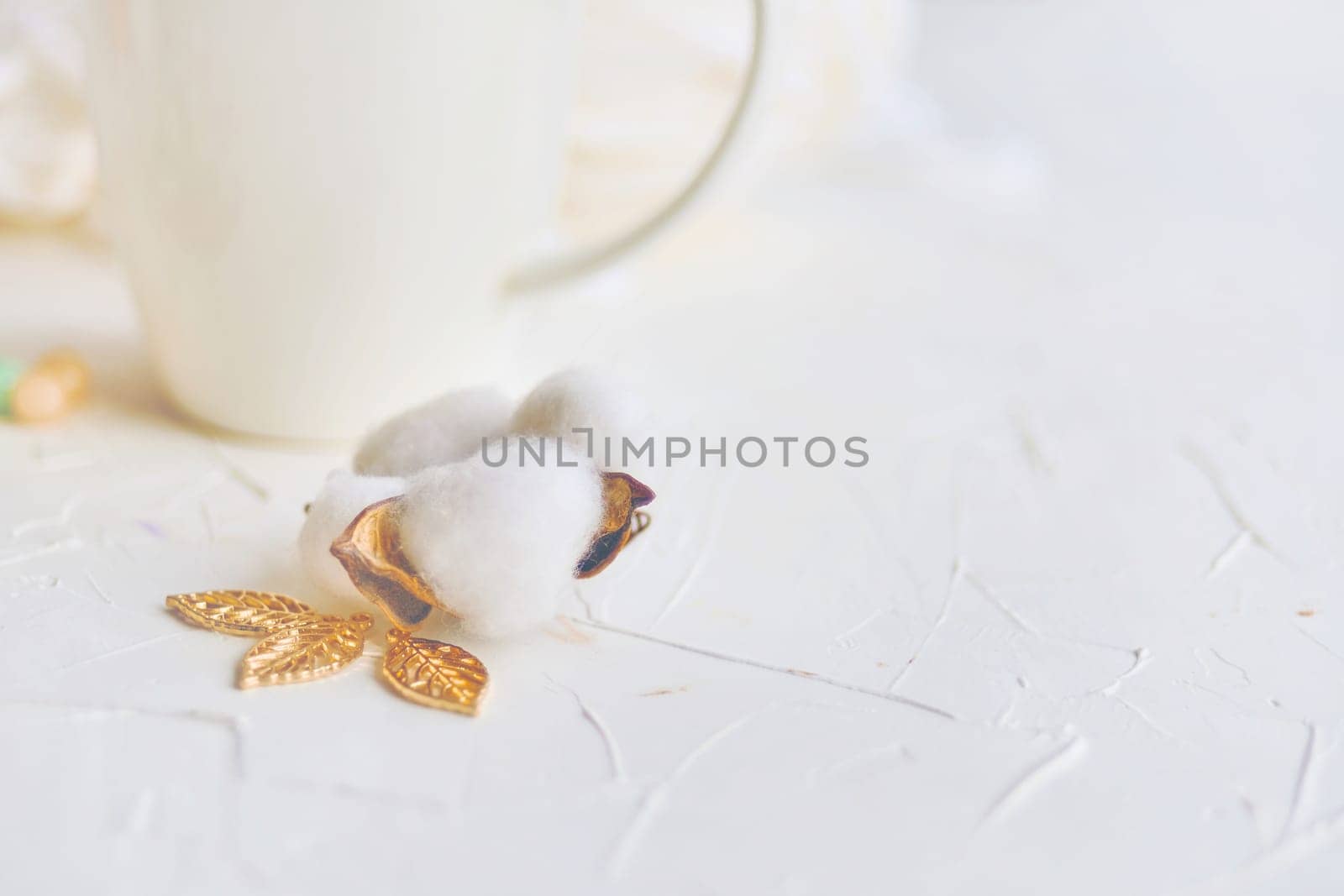 Serene atmosphere with white background, cotton flower, and golden leaves creates a refined setting