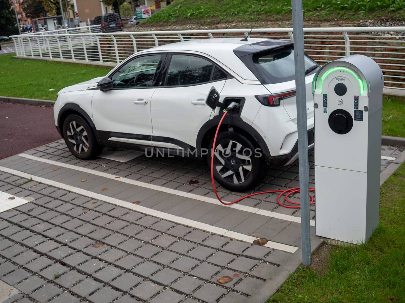 Cremona, Lombardy, Italy October 15th 2024 Modern white electric car charging its battery at a public charging station, promoting sustainable transportation and eco friendly practices