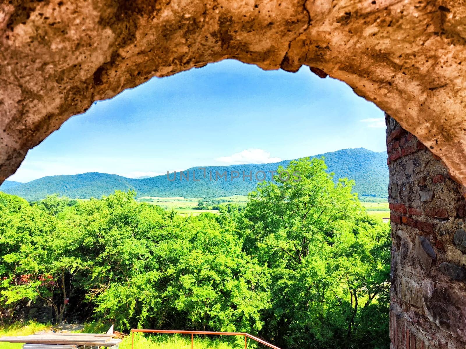 Lush greenery and rolling hills are visible beyond a weathered stone arch.