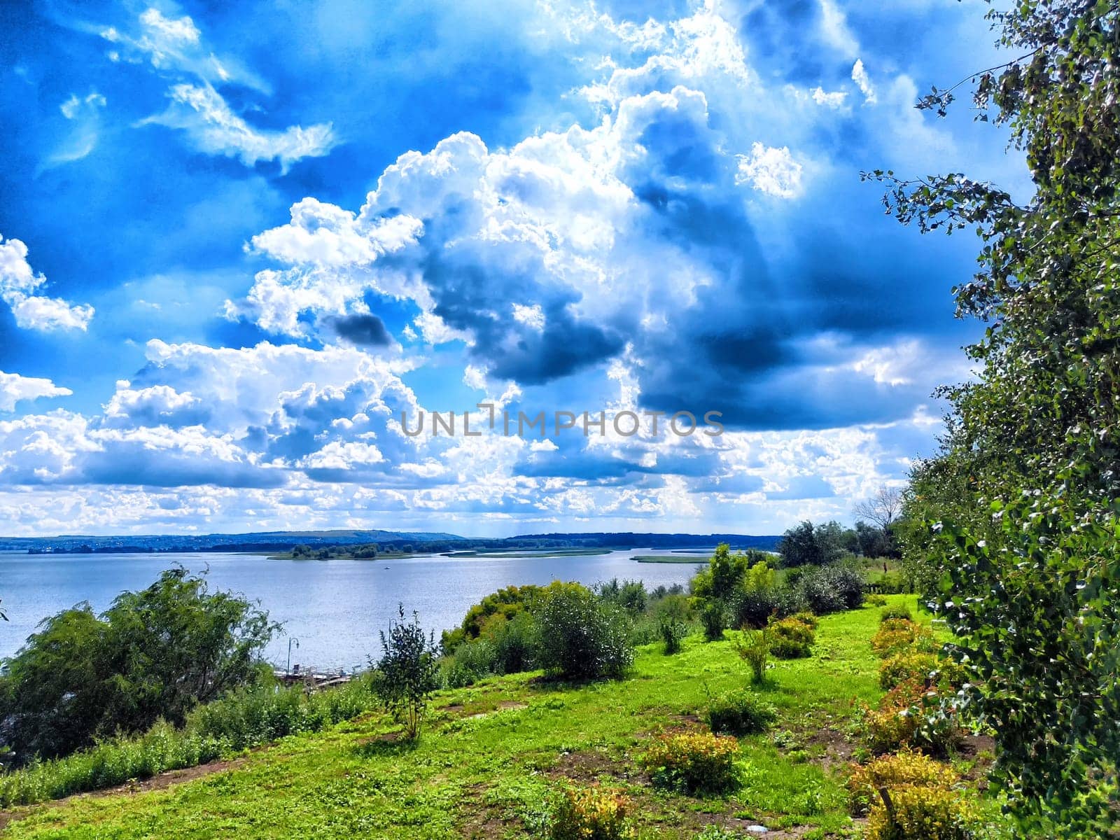 The view reveals lush greenery lining a riverbank under a stunning blue sky filled with clouds.