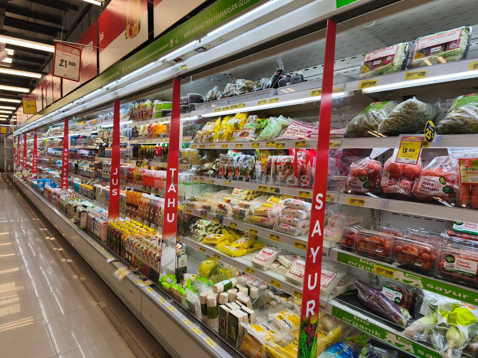 A well stocked refrigerated section in a grocery store, showcasing a variety of fresh vegetables, mushrooms, and fruits.
