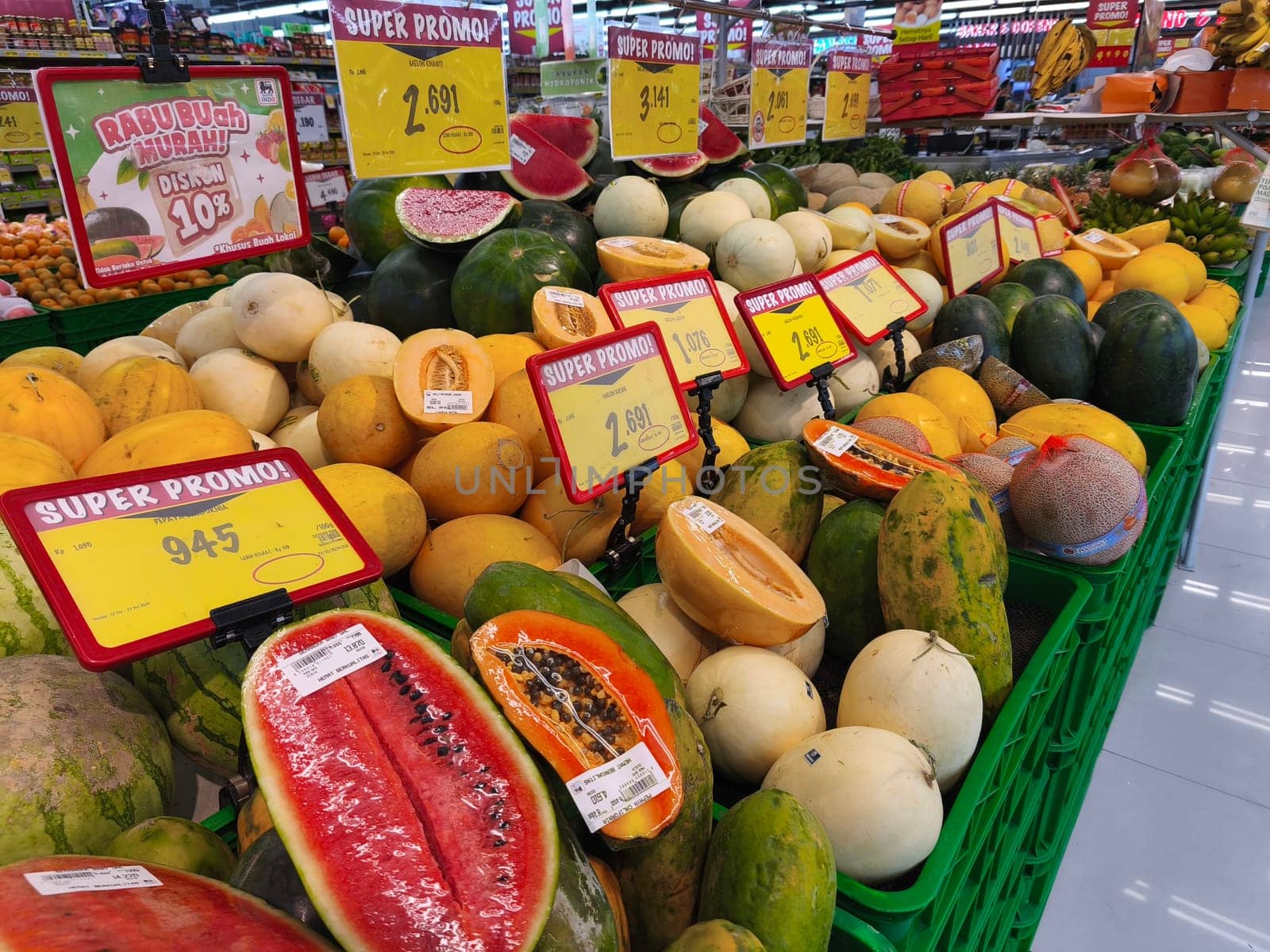 October 22, 2024. Surabaya, Indonesia. A fruit stand with a variety of fruits on display, including watermelons, cantaloupes, honeydew melons, and papayas. There are signs advertising SUPER PROMO and discounts.