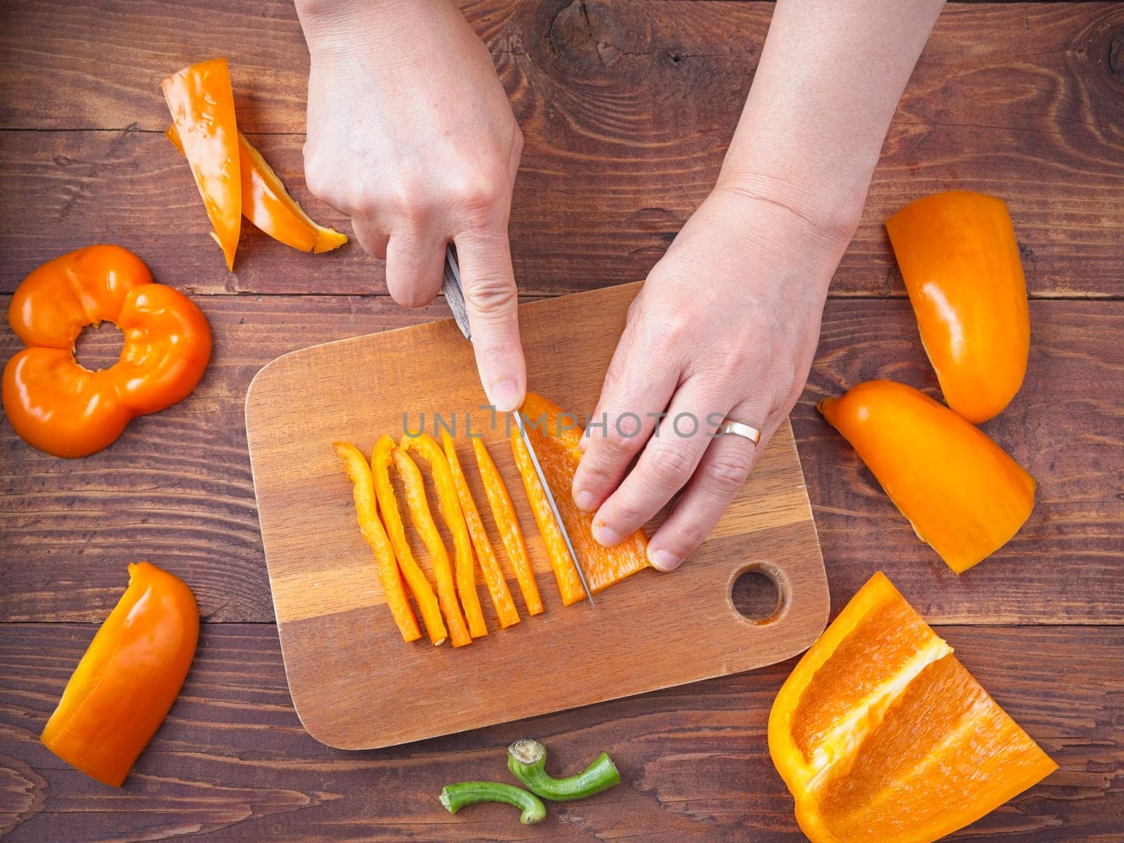 A flatlay photo of hands cutting orange bell peppers in a studio setting.