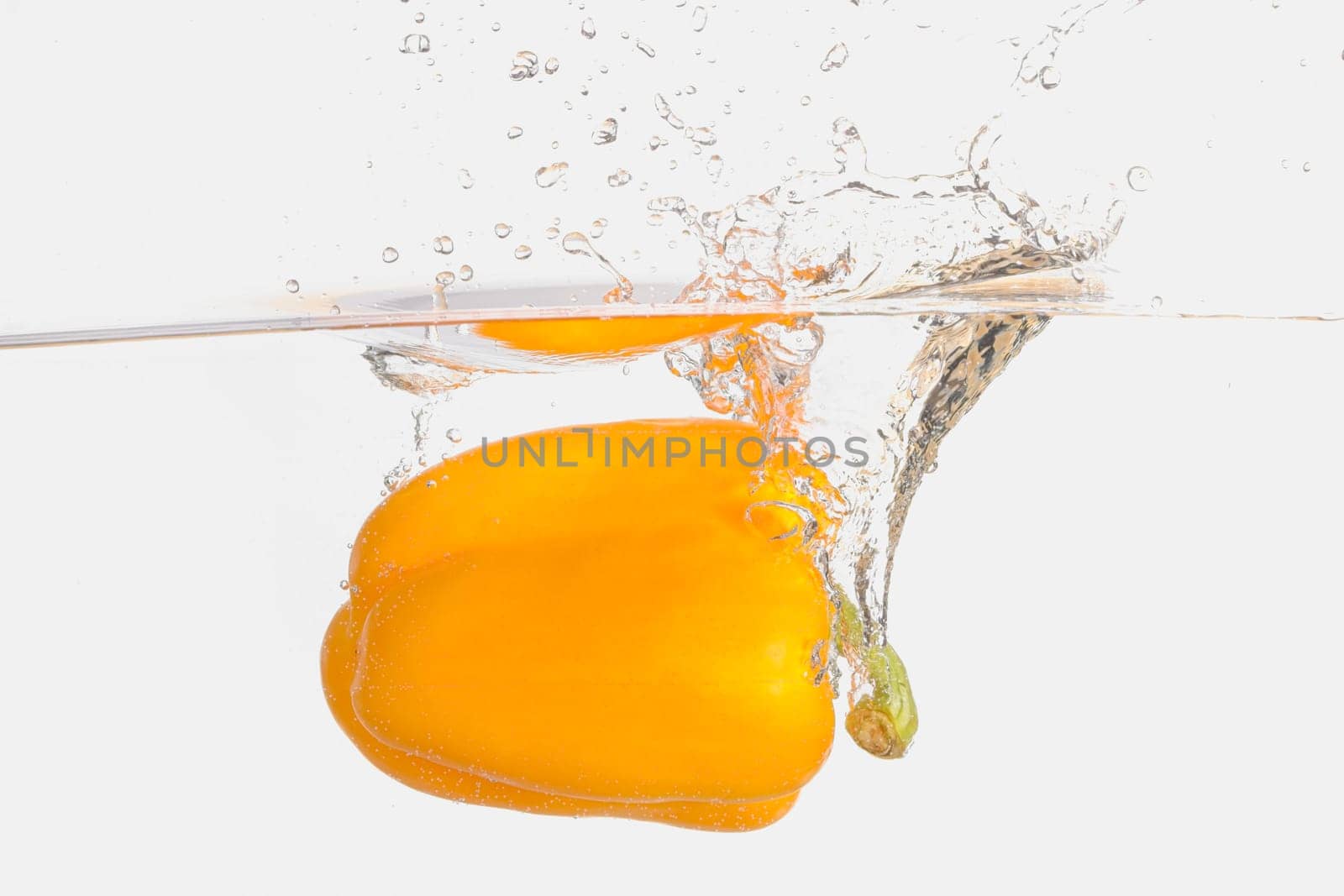 A large orange bell pepper making a splash after being dropped in water in this studio photo.