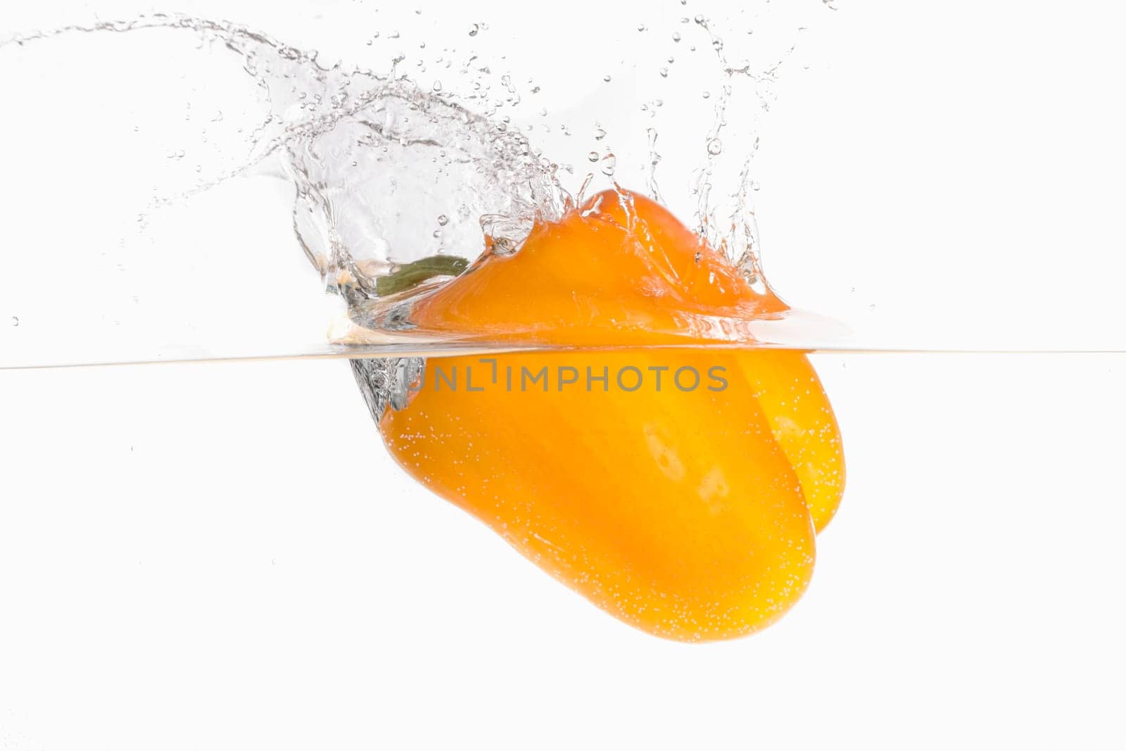 A large orange bell pepper making a splash after being dropped in water in this studio photo.