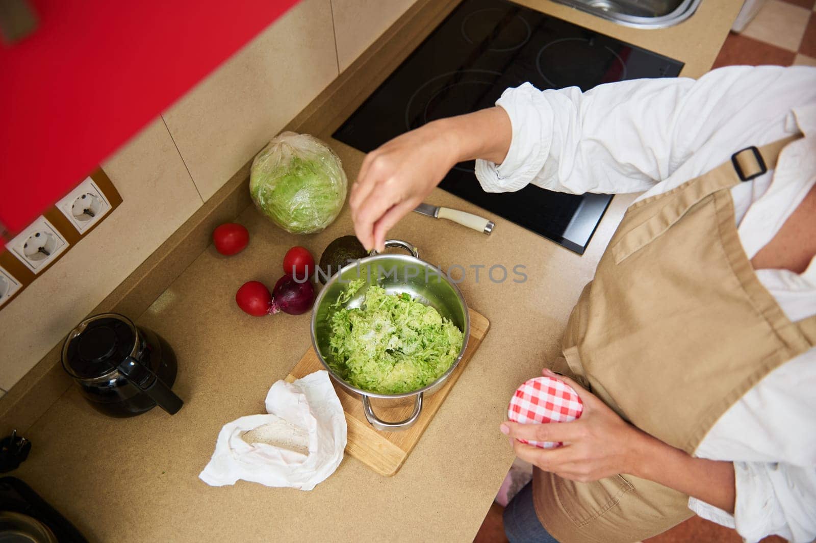 A top view of a woman in an apron preparing a fresh salad in a modern kitchen. Surrounded by fresh ingredients like lettuce and tomatoes, she combines nature's best for a healthy meal.