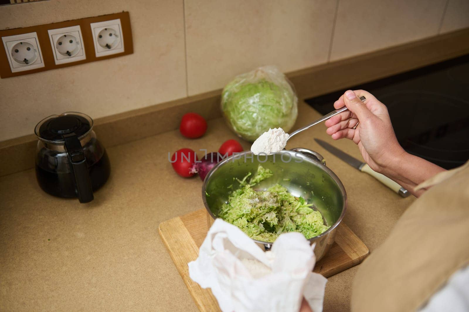 A person is preparing a dish by adding flour to a bowl of mixed vegetables on a countertop with fresh ingredients nearby.