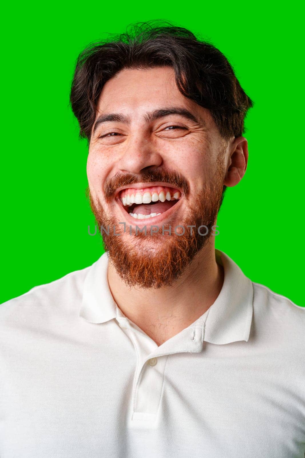A smiling young man with a beard poses against a bright green background close up