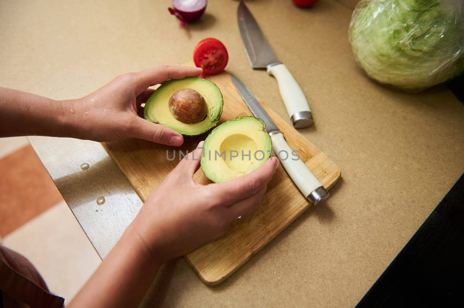 A person slices an avocado on a wooden board in a kitchen, surrounded by ingredients. The scene is vibrant, emphasizing healthy eating and food preparation. Ideal for culinary themes.