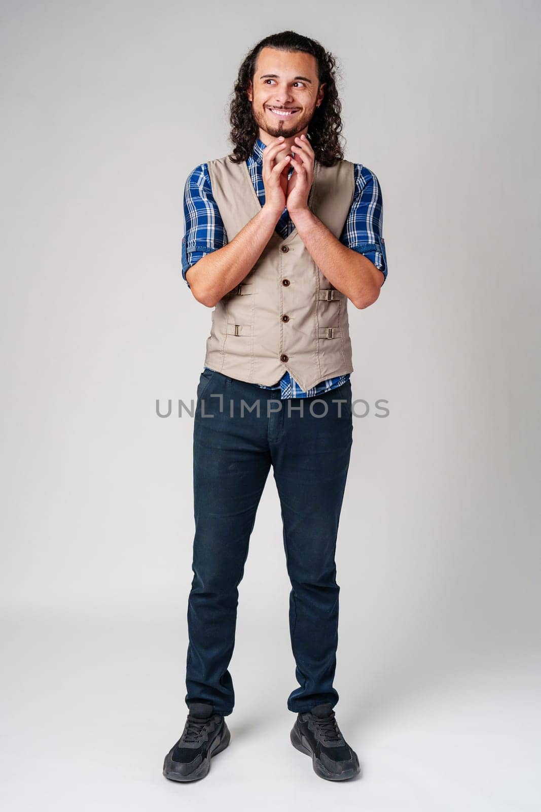 Man in a plaid shirt and vest stands smiling, looking optimistic in a neutral studio setting close up
