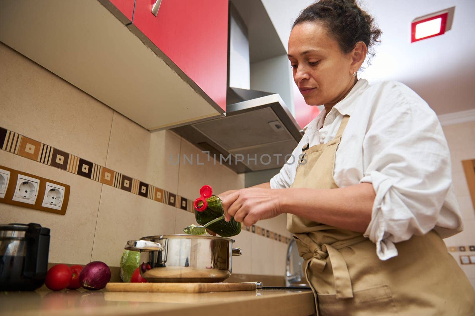 A woman in an apron is seen preparing a healthy meal in her kitchen, focusing on fresh vegetables. The image conveys a sense of domestic calm and culinary passion.