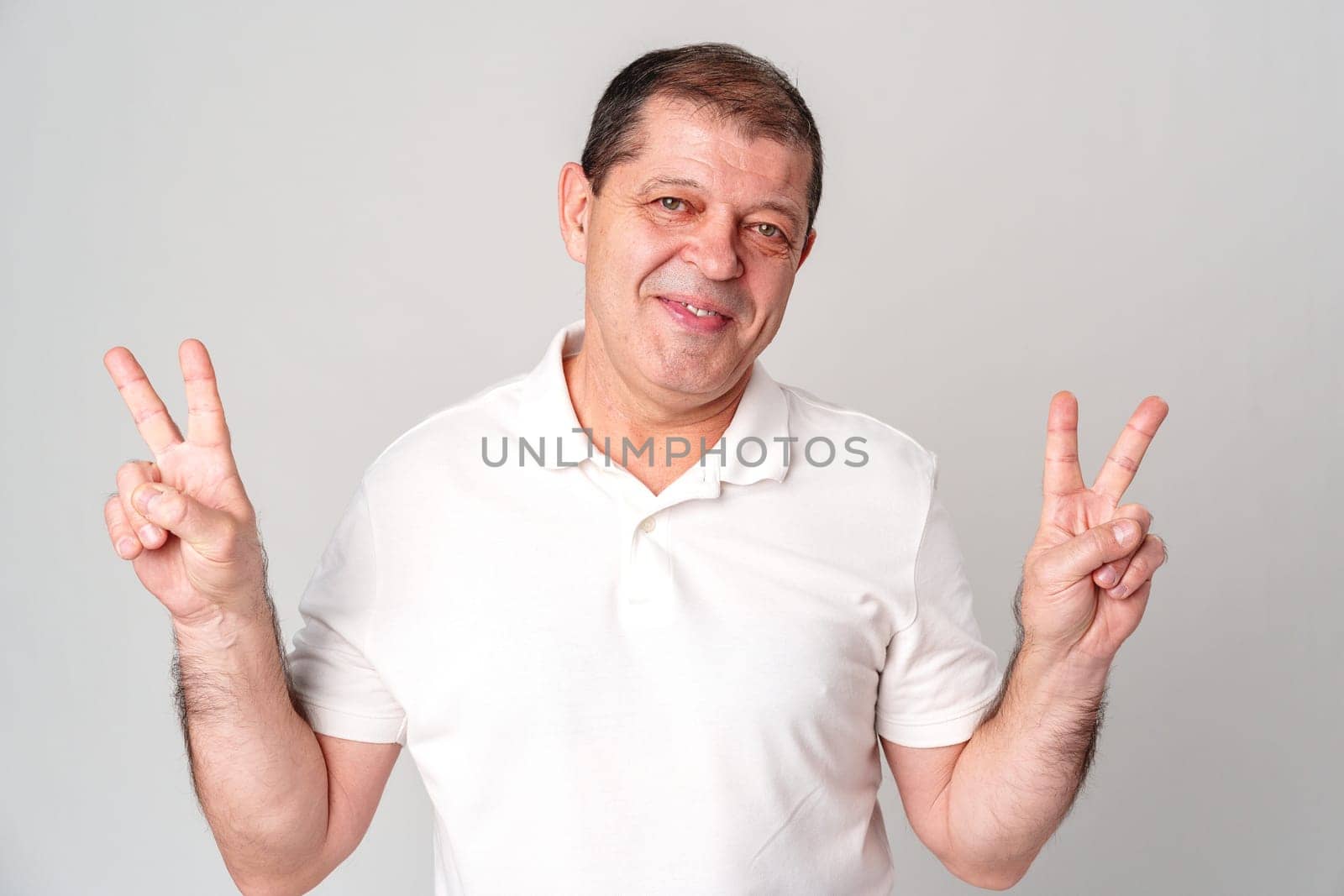 Man wearing a white shirt making peace signs with his hands against a plain background close up