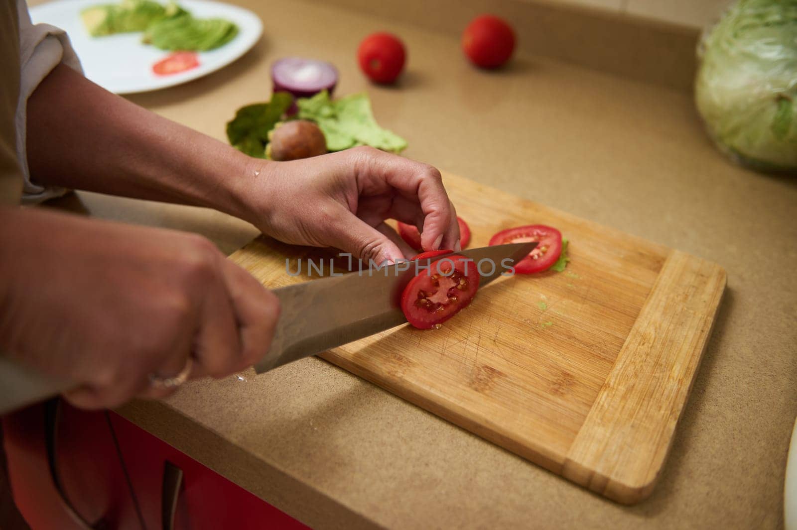 A person expertly slices ripe tomatoes on a wooden cutting board, surrounded by fresh vegetables. Perfect for illustrating healthy cooking or recipe preparation in a kitchen setting.