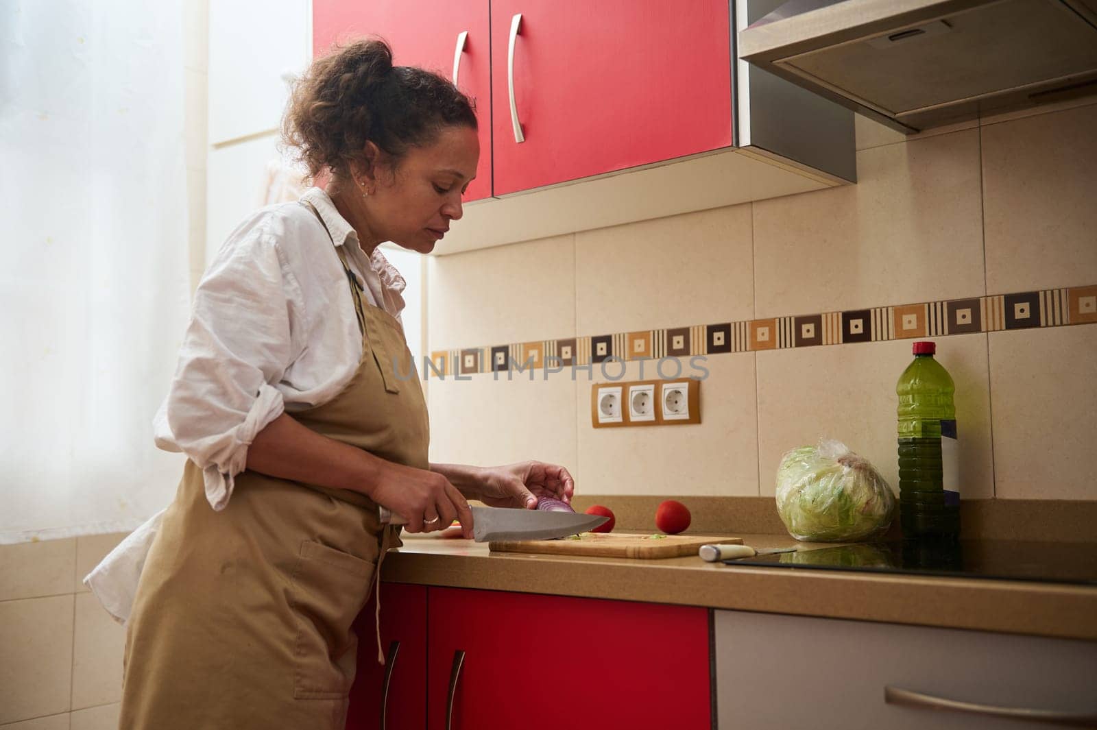 A woman confidently chops vegetables in a modern kitchen, focusing on preparing a nutritious meal. The scene exudes warmth and culinary passion.