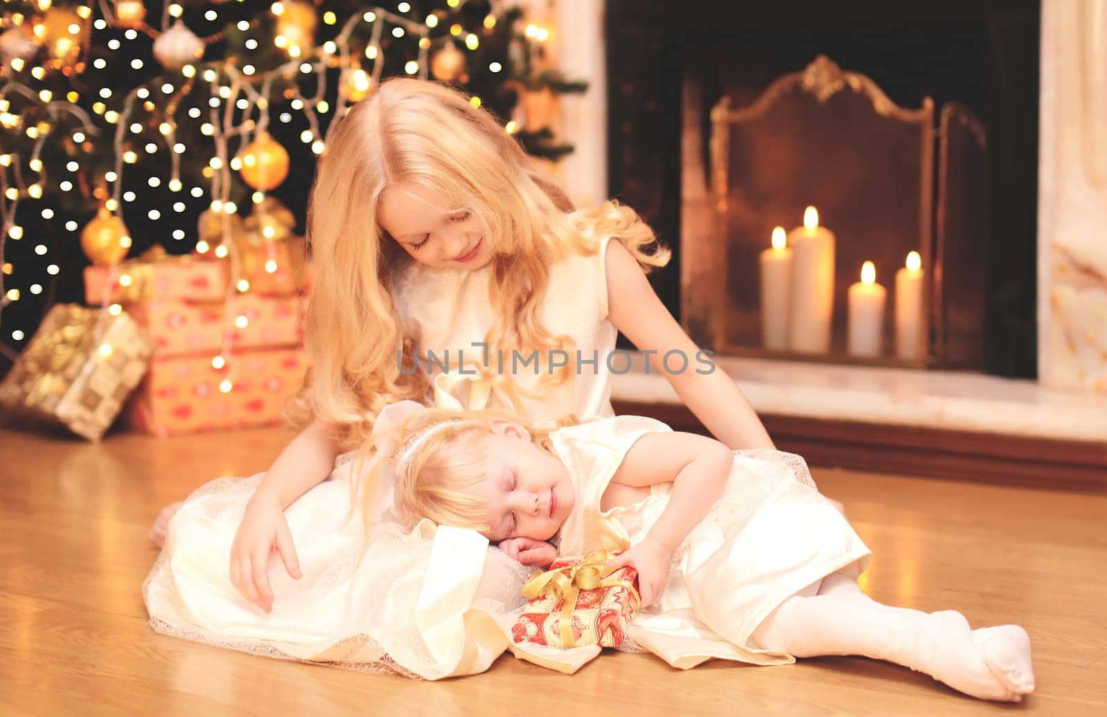 child little girl gives a gift box to sister over christmas tree and  fireplace at home