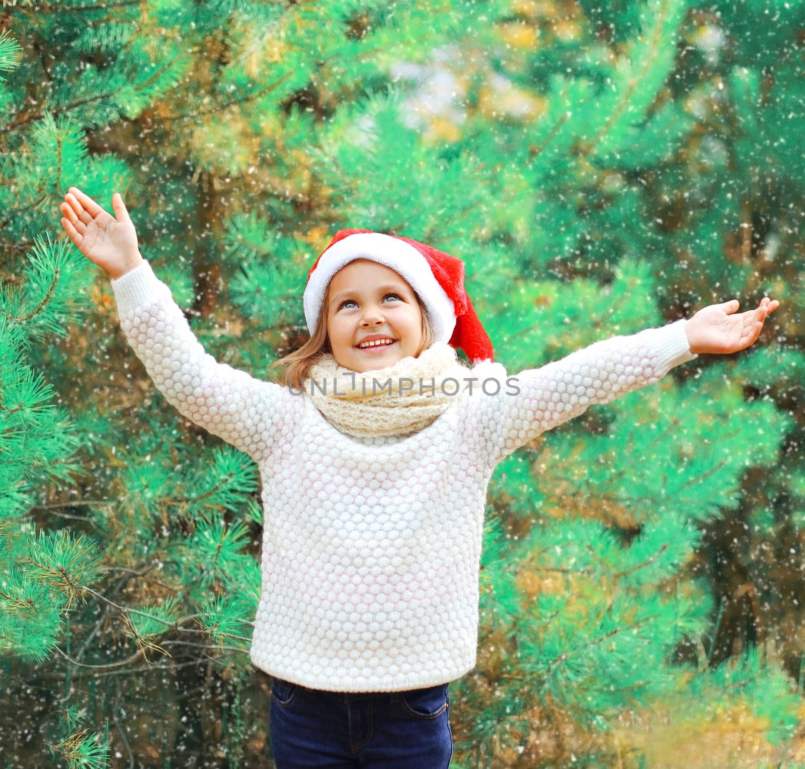 Christmas smiling child little girl in santa red hat over a tree having fun