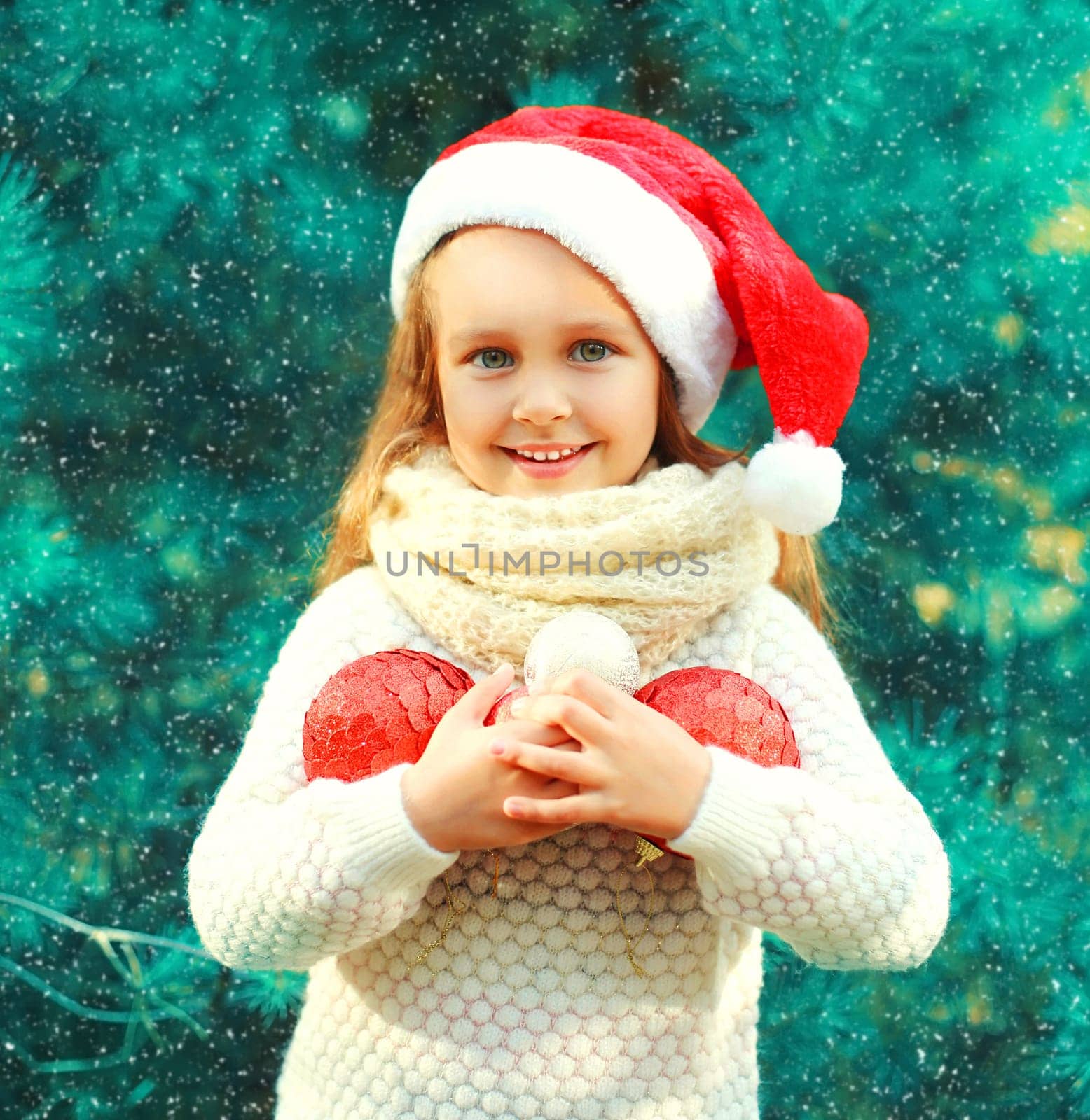 Christmas smiling child little girl in santa red hat with many balls near a tree