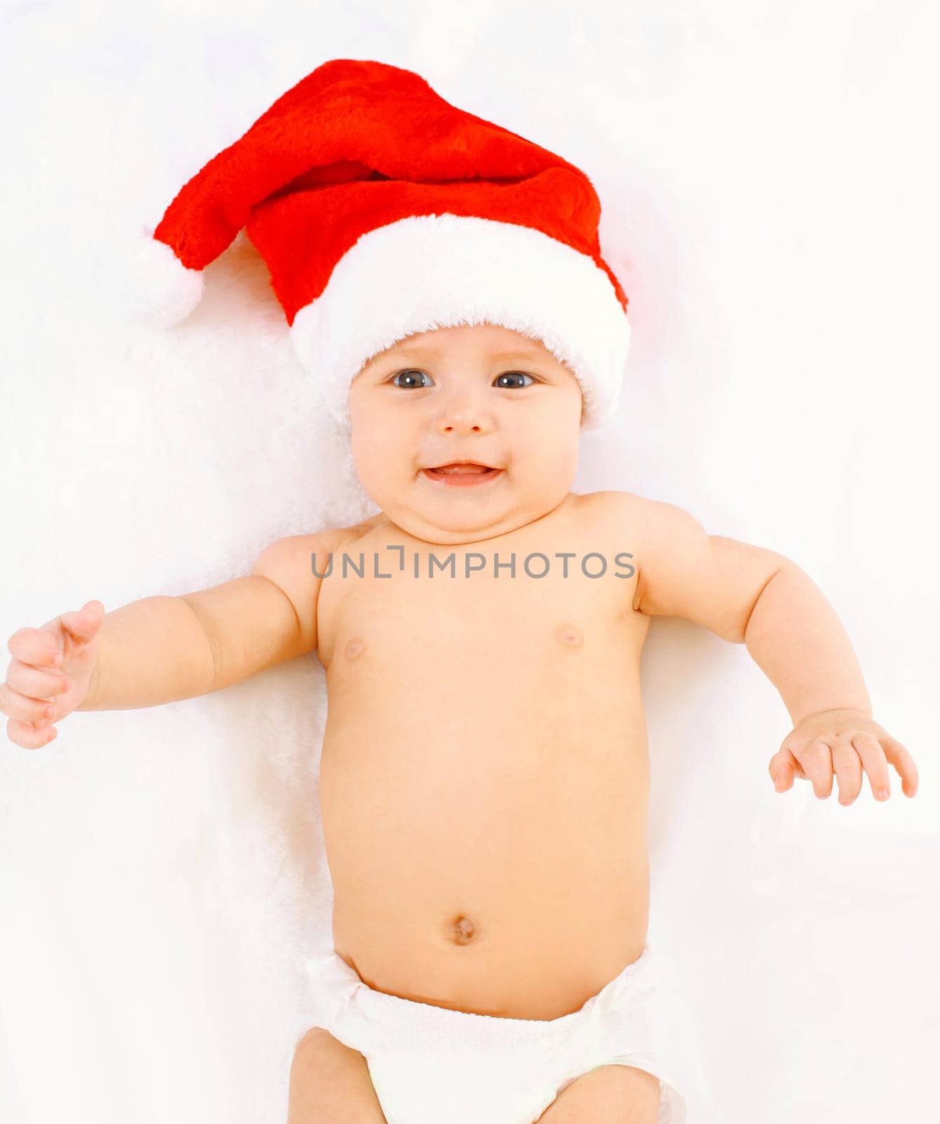 Christmas, family concept - cute baby in red santa hat lying on white bed at home