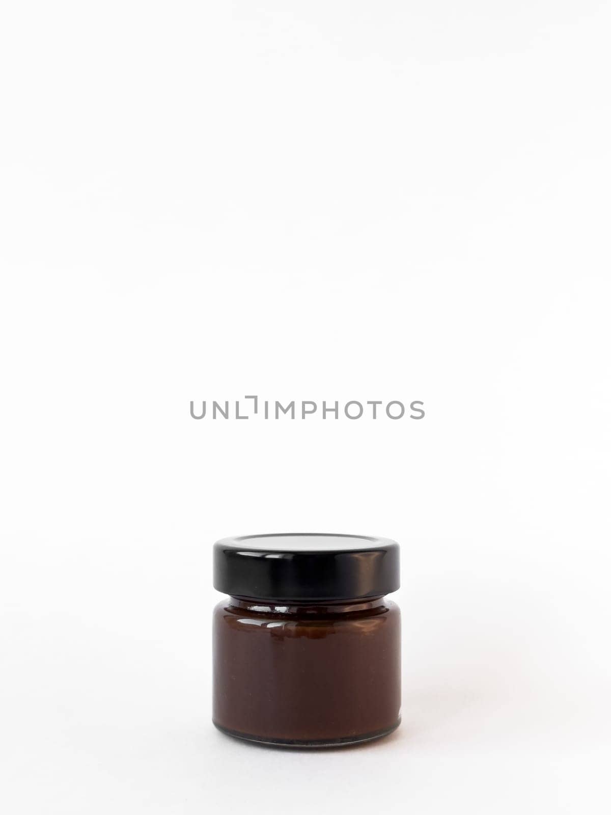 Minimalist display of a small brown glass jar with black lid on white background.