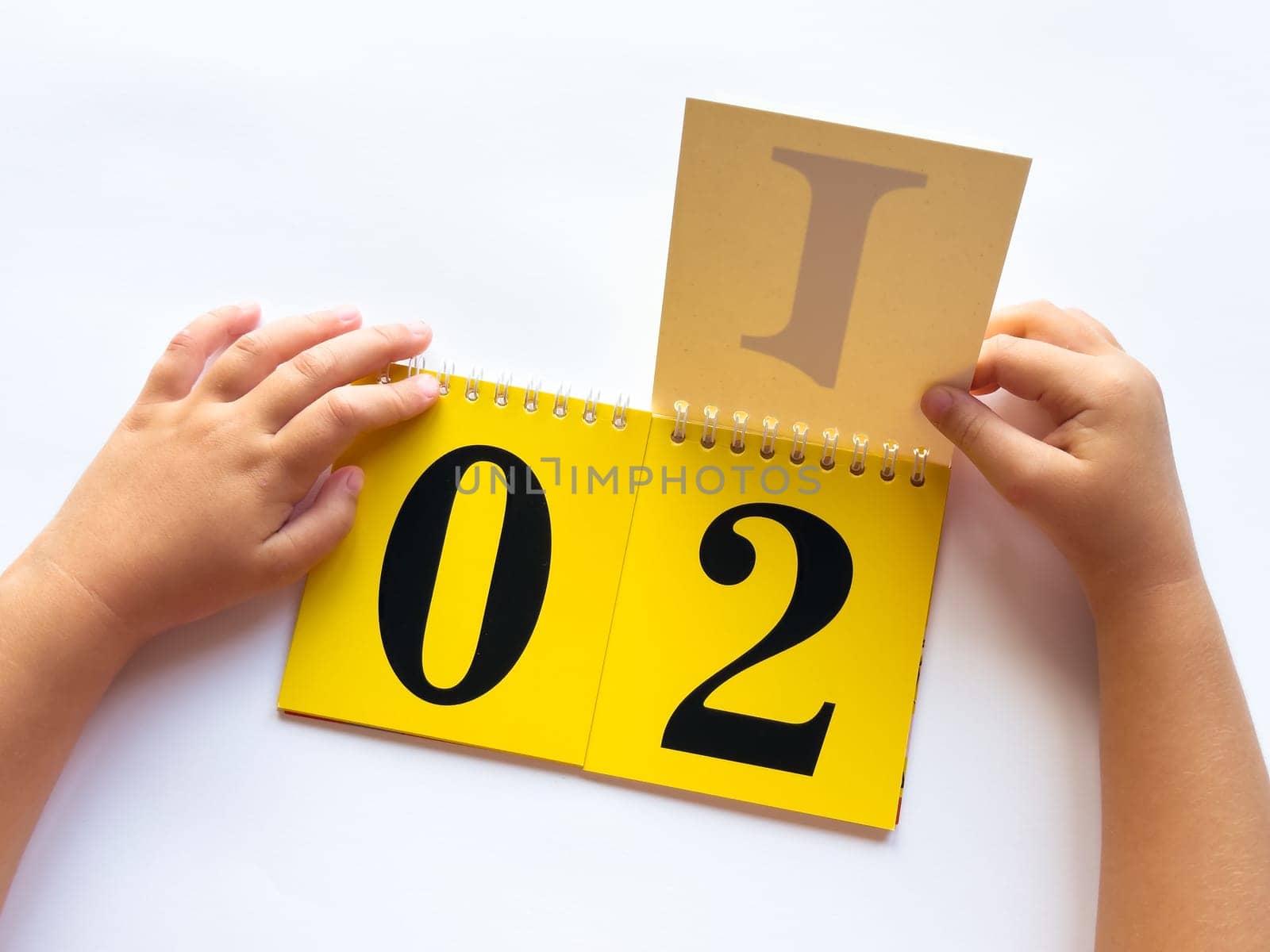 Childs hands flipping educational flashcards with numbers and letters on bright yellow background.