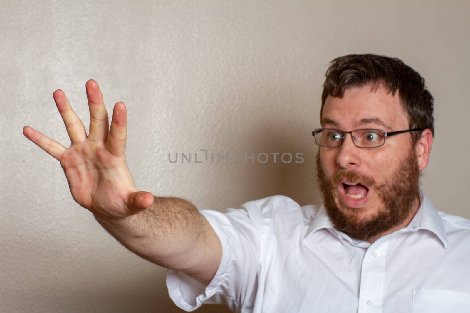 A bearded man wearing glasses and a white shirt expresses surprise while reaching out with his hand. The moment captures curiosity and unexpected reaction.
