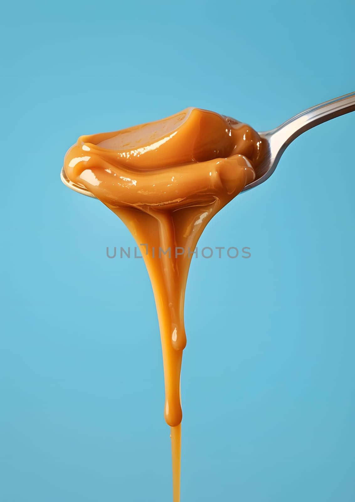 Caramel sauce dripping off a spoon on blue backdrop, delicious and sweet.