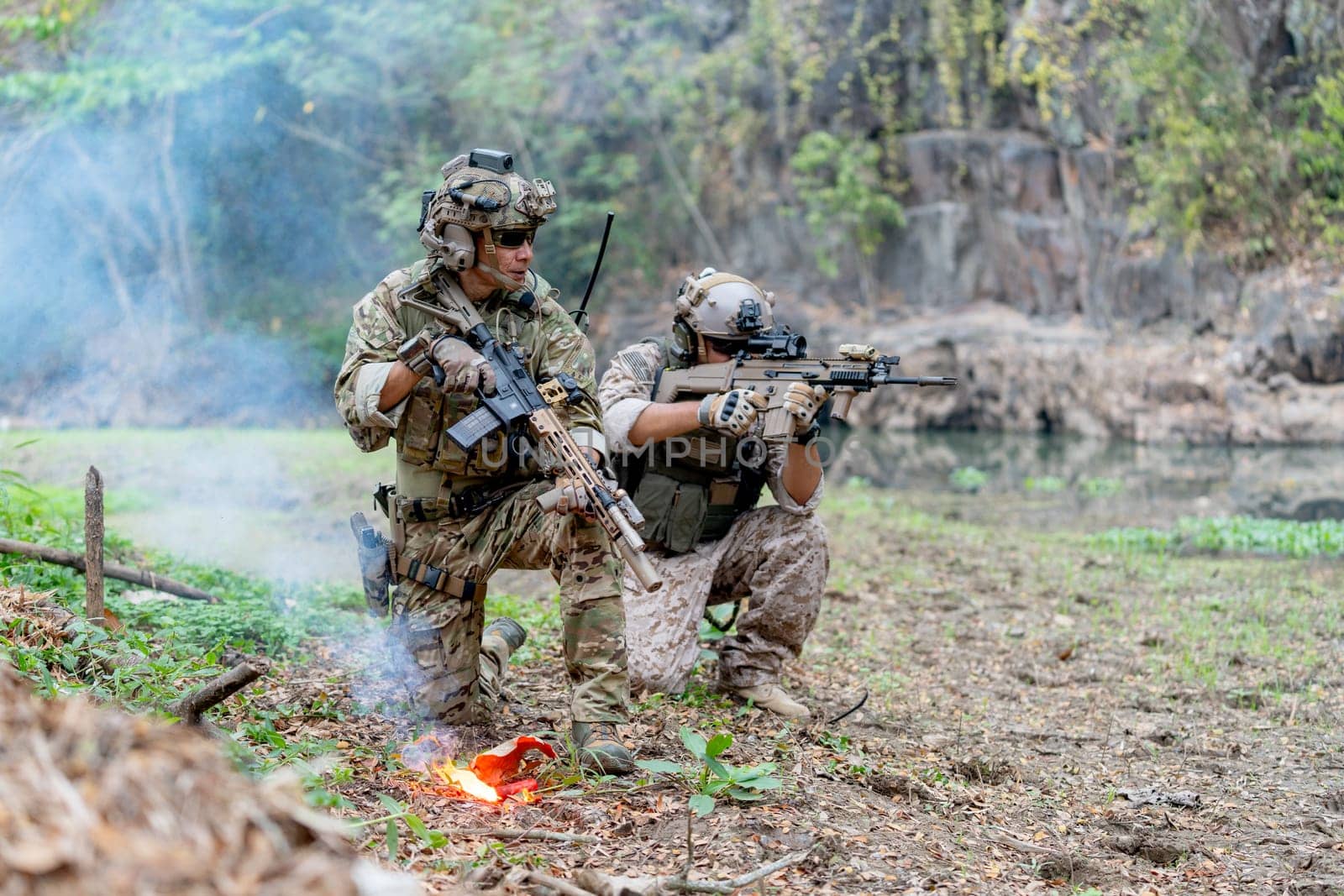 Militaries or soldiers stay in battlefield near the river with holding gun also one point gun forward direction during outdoor practice in front of flare.