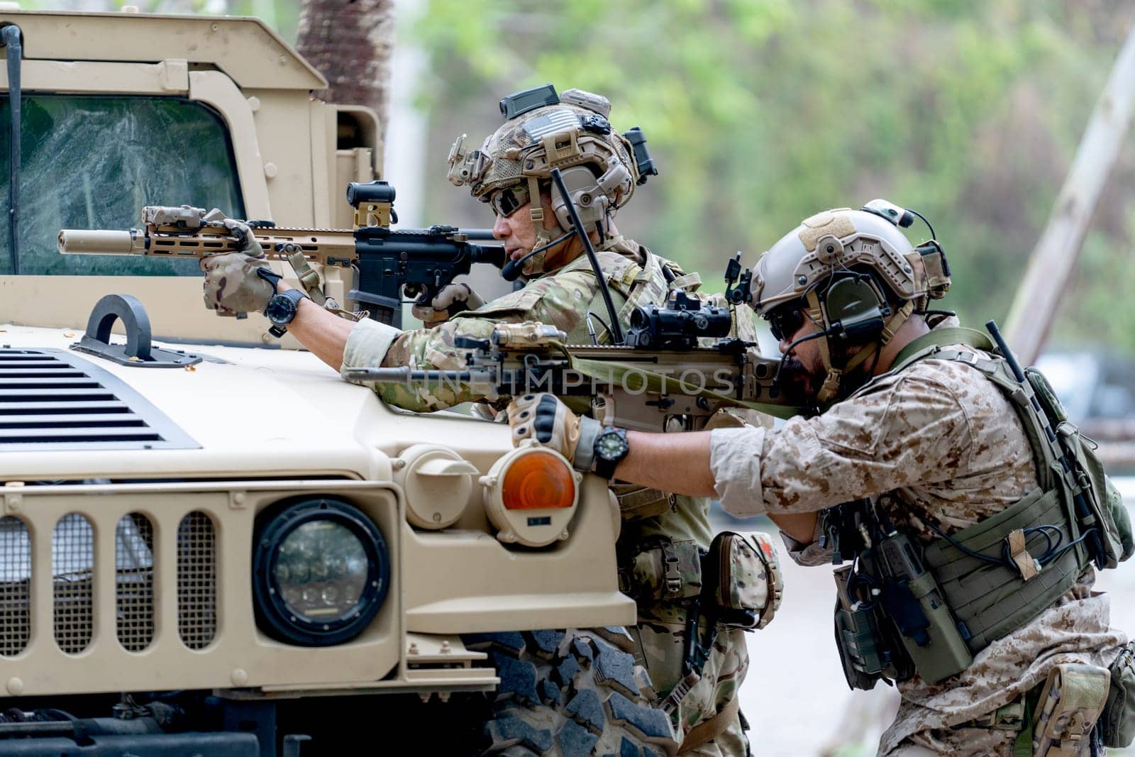 Two militaries or soldiers stay in front of humvee car area of car hood and point gun to left side during outdoor practice.