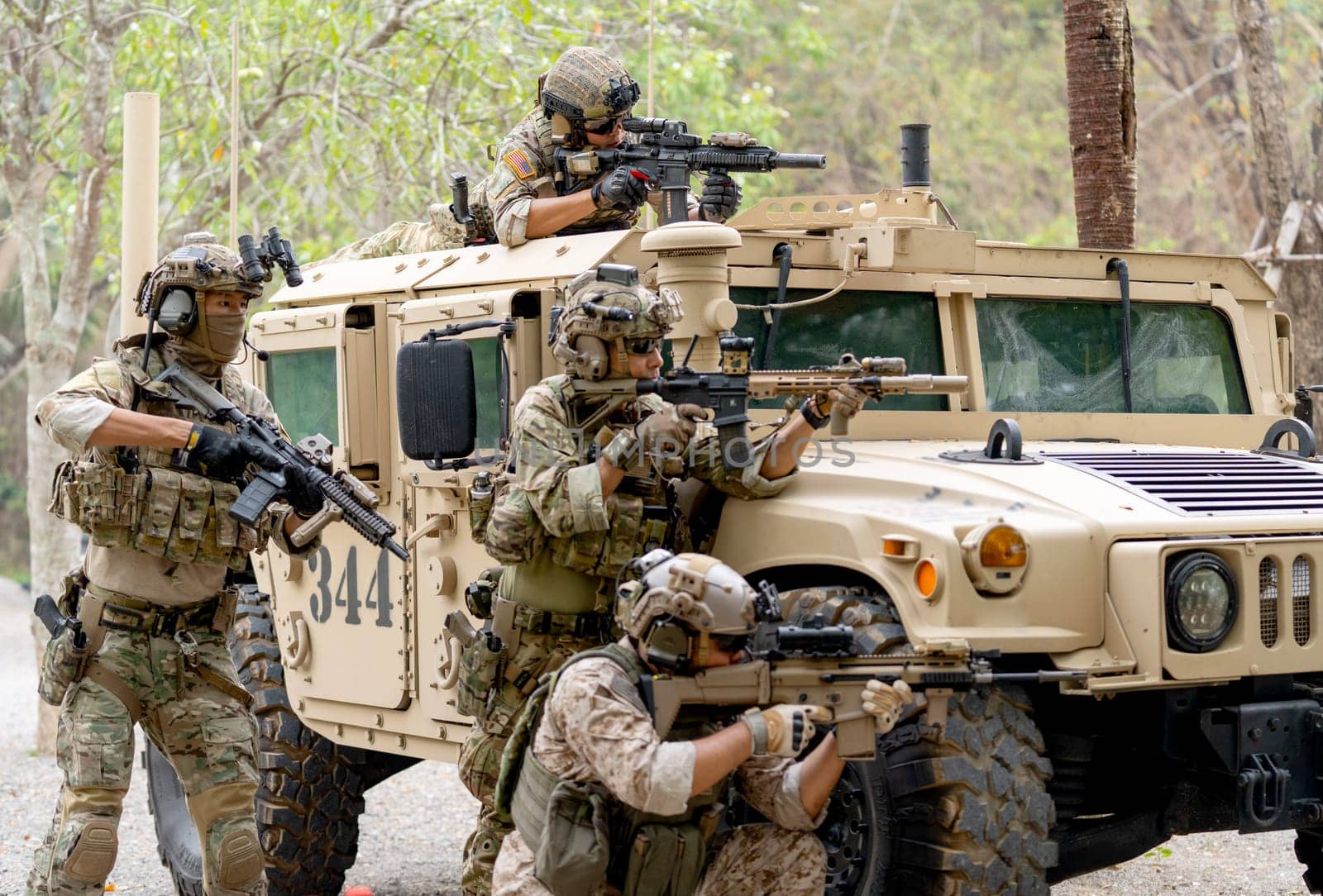 Group of militaries or soldiers stay near humvee car with one on roof and the other stay in area of car hood also point gun to right side during outdoor practice.