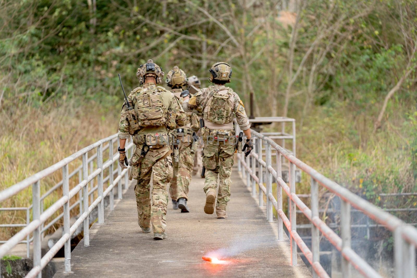 Back of military or soldier team with battle suit walk on the bridge near flare firework during outdoor practice.