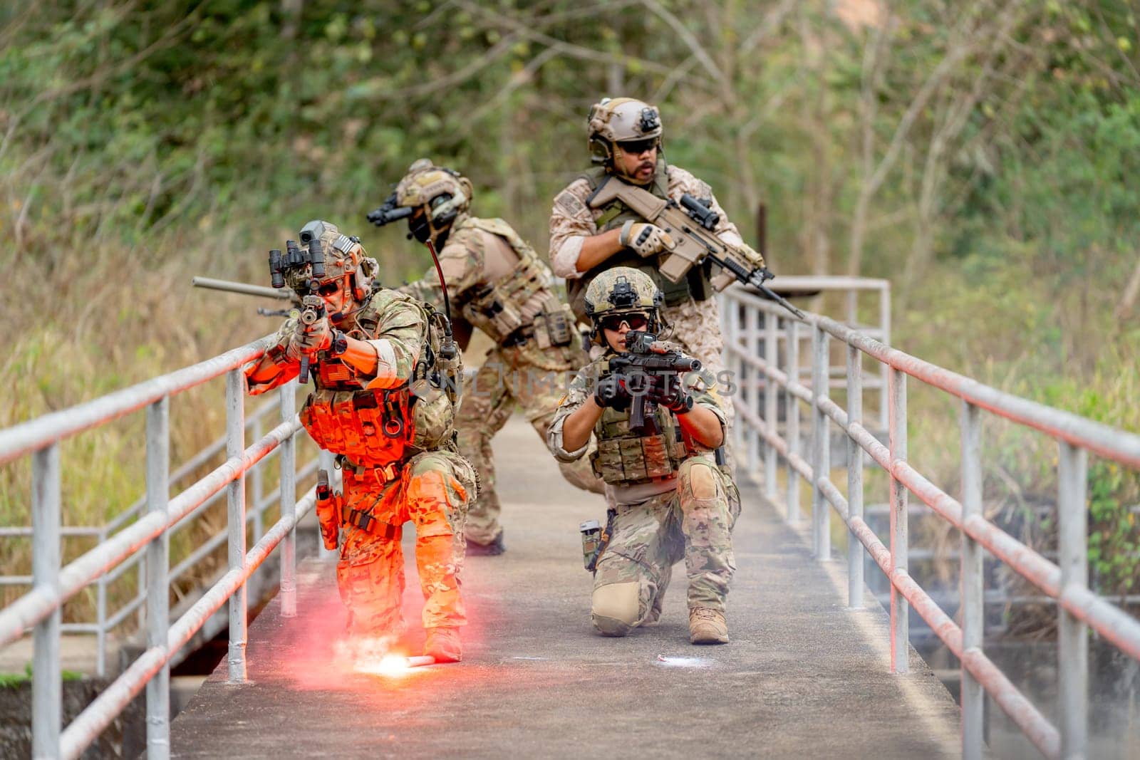 Group of military or soldier team with battle suit stay on the bridge near flare firework in position for battle and point gun different direction during outdoor practice.