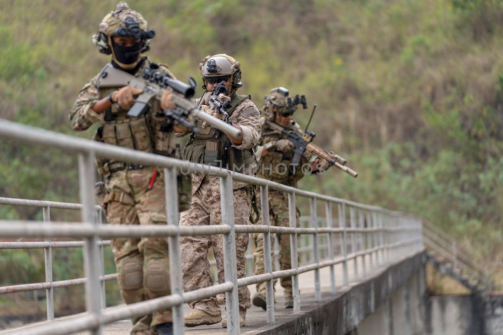 Side view group of military or soldier team with battle suit stand on the bridge and point gun down direction to enemy during outdoor practice.