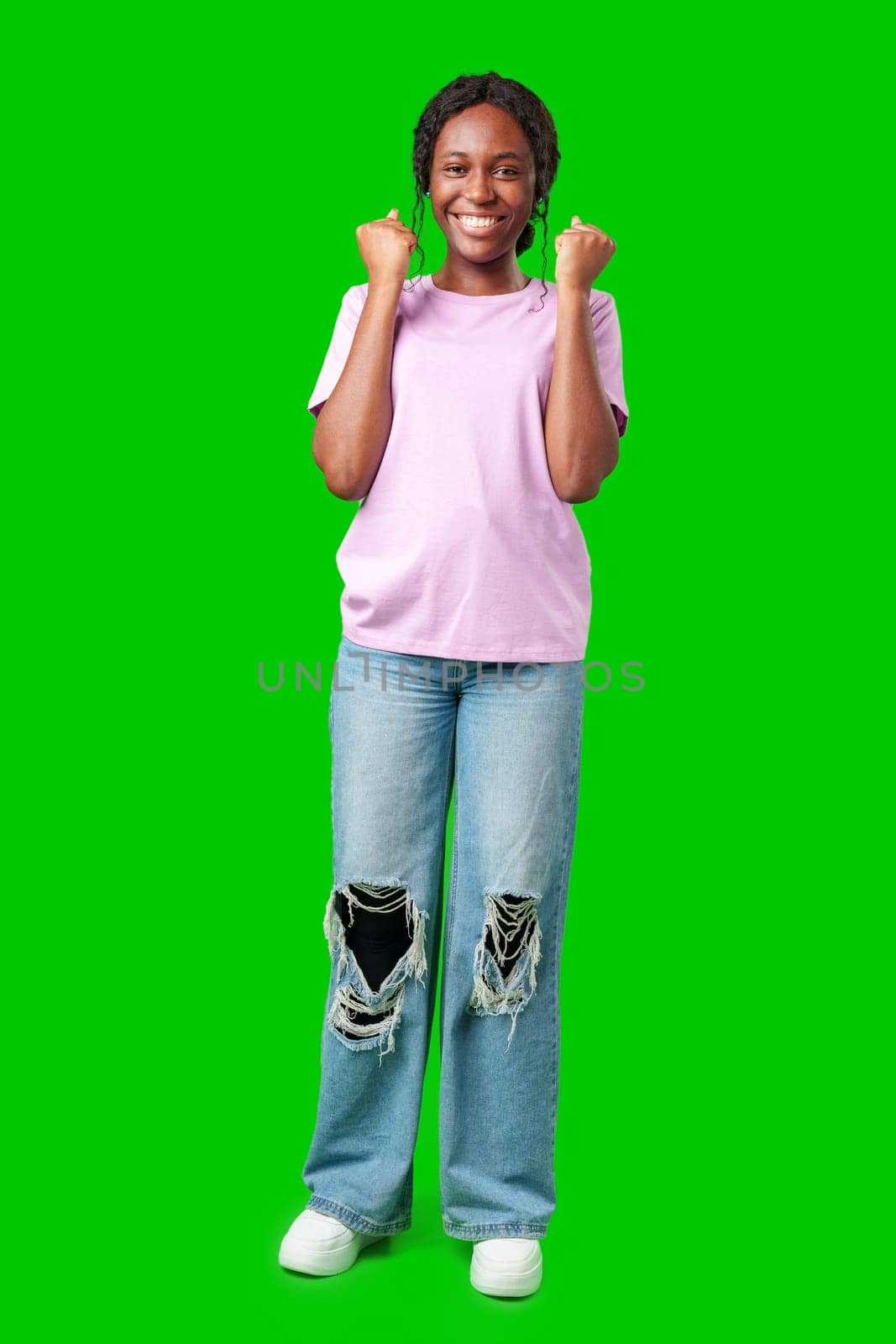 A young woman with braids expresses excitement with a clenched fist against a bright green background in studio