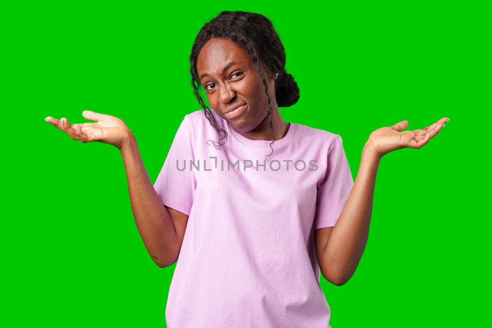 A young woman in casual attire smiles playfully with hands raised in a questioning gesture against a bright green background close up