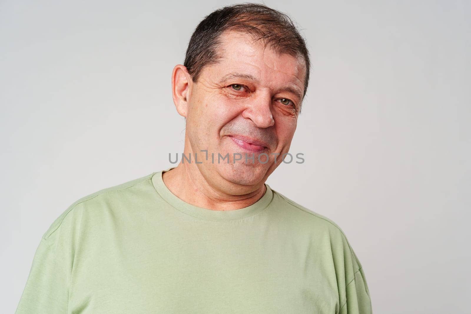 Friendly older man smiling warmly in a light green shirt against a neutral background close up