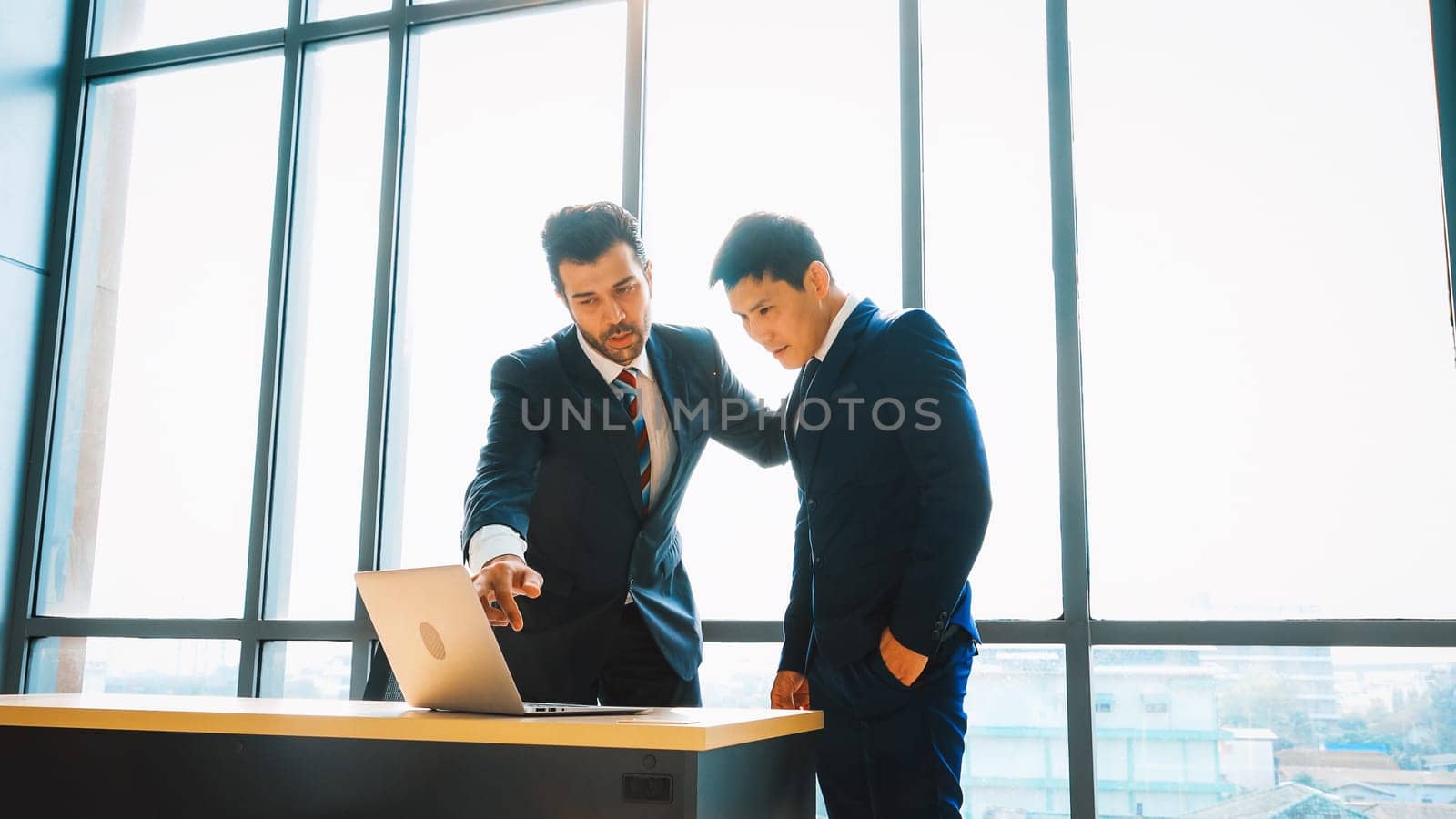 Two business people talk project strategy at office meeting room. Businessman discuss project planning with colleague at modern workplace while having conversation and advice on financial report. Jivy