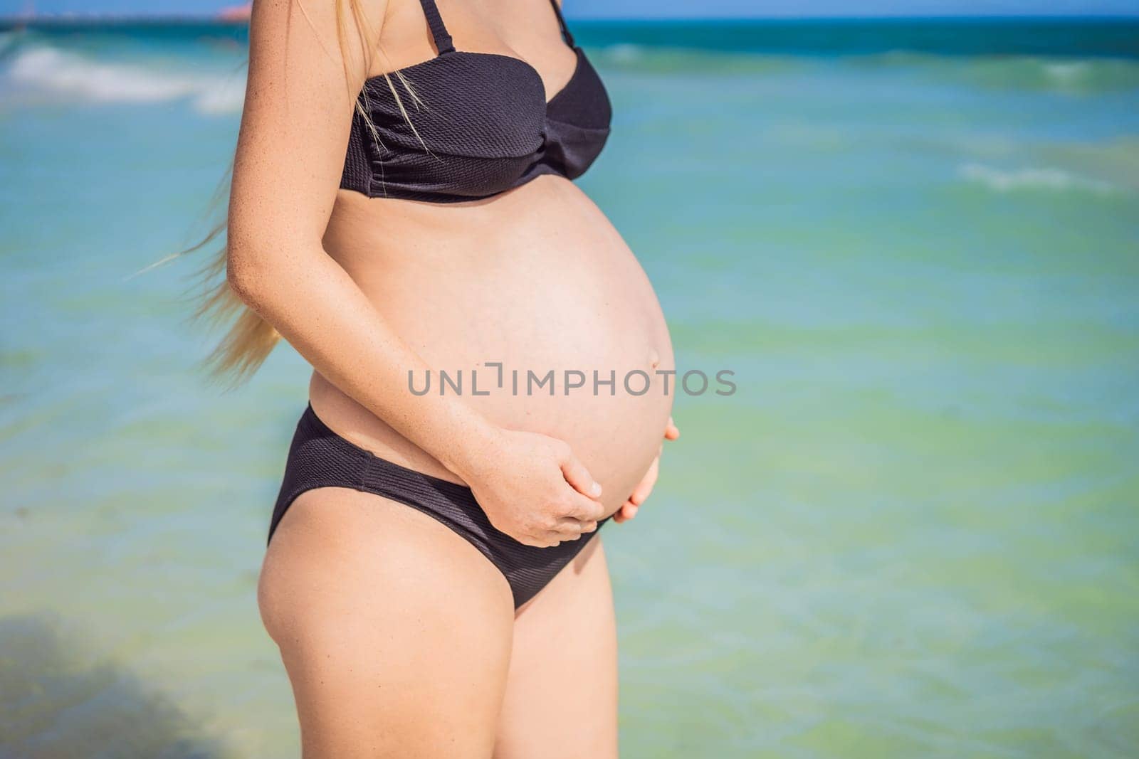 Radiant pregnant woman in a swimsuit, amid the stunning backdrop of a turquoise sea. Serene beauty of maternity by the shore.