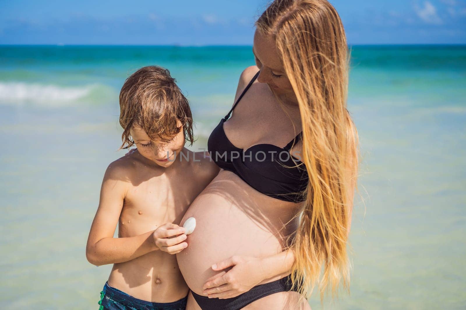A picturesque moment: a pregnant woman and her son enjoying the turquoise sea, a heartwarming family bond by the tranquil shore.