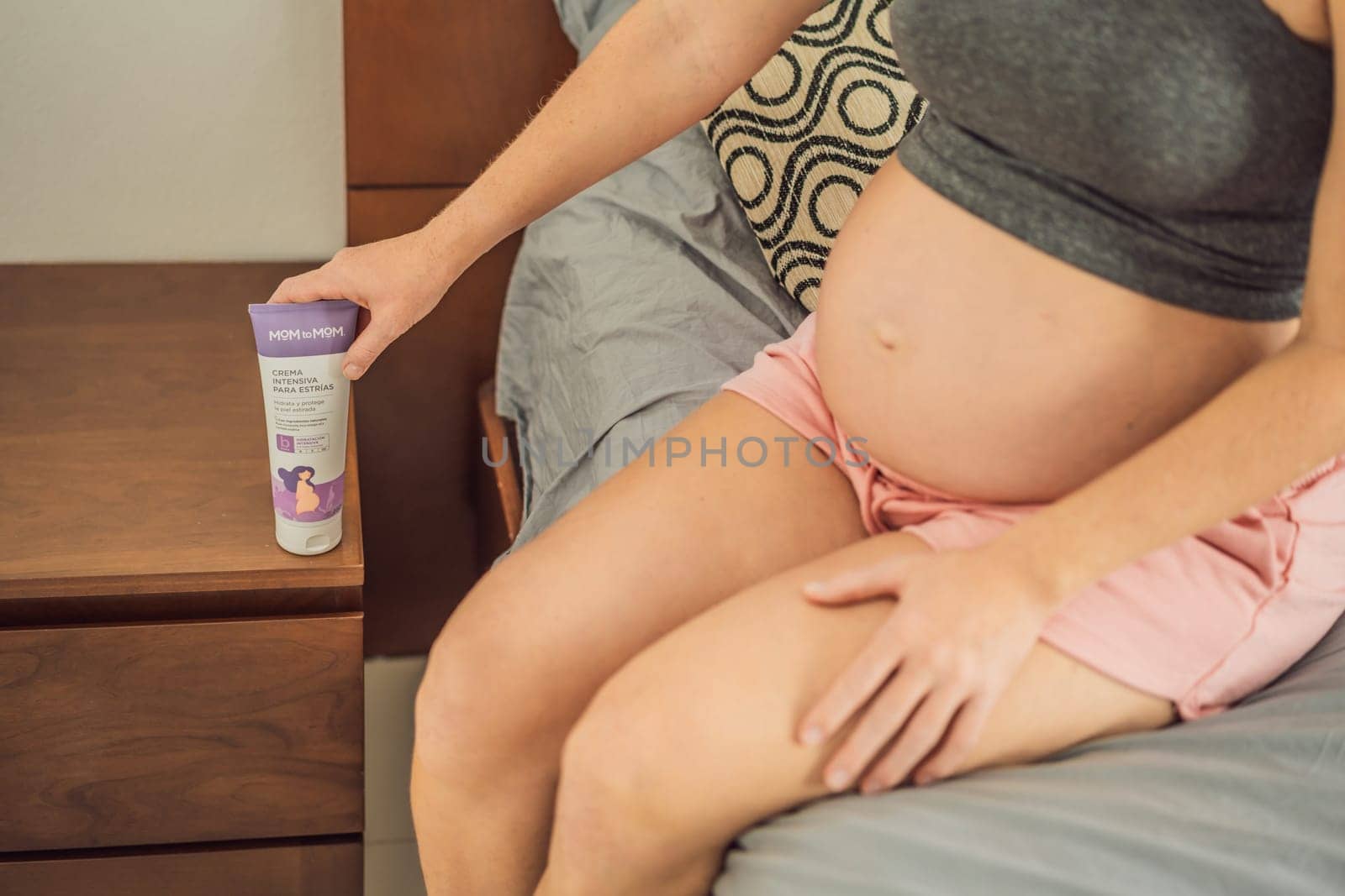 Mexico, Cancun, 02.02.2022: Mom to mom cream for stretch marks for pregnant women. Positive young pregnant woman in comfortable homewear applying belly butter on her big tummy, woman belly by galitskaya