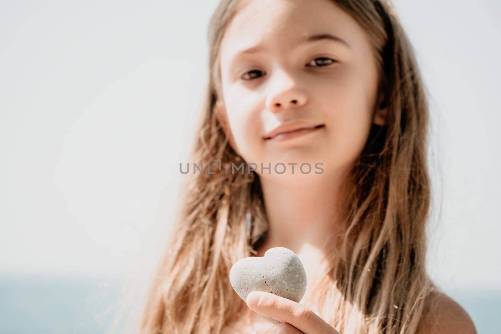 Female hand holding a stone in the shape of a heart against the background of the sea