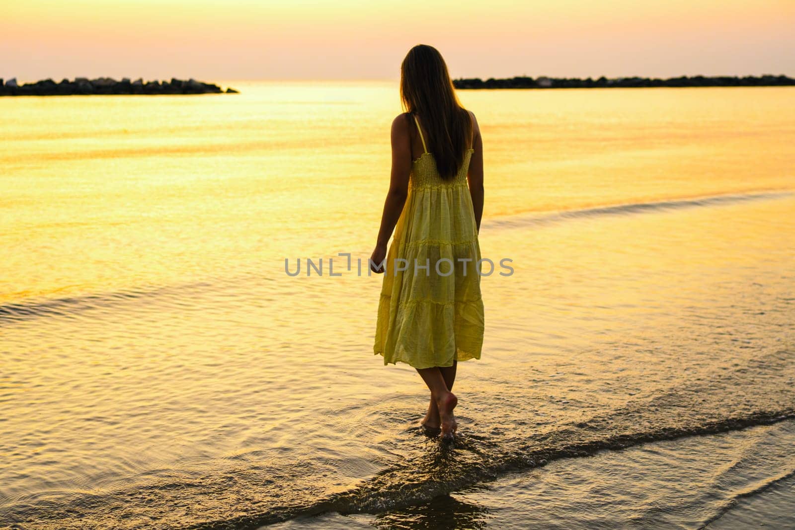 A young woman stands on the beach watching the sunrise.