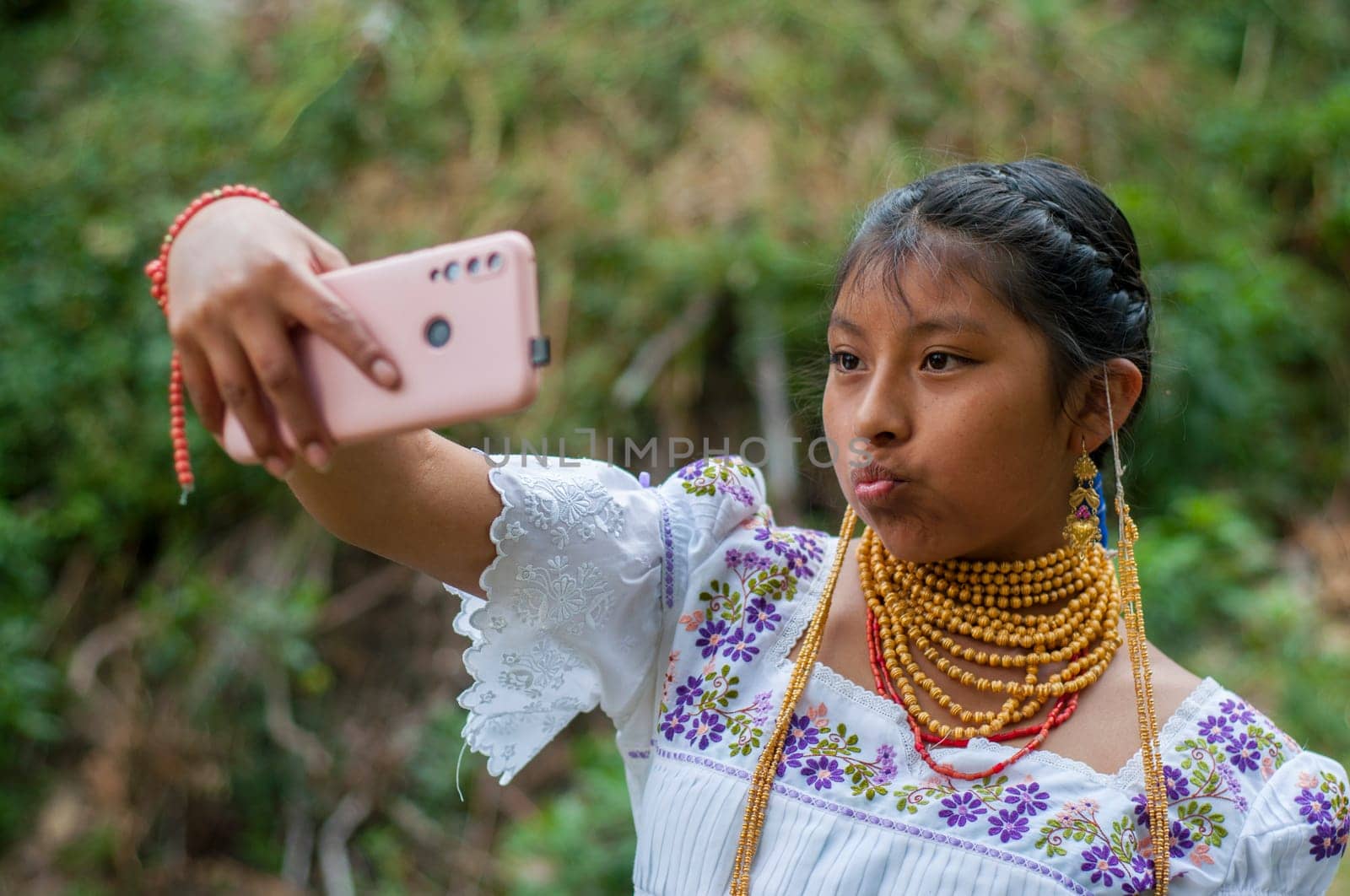 INDIGENOUS YOUNG MAN smiling in the middle of nature taking a selfie with a cell phone wearing clothes from his native community. by Raulmartin