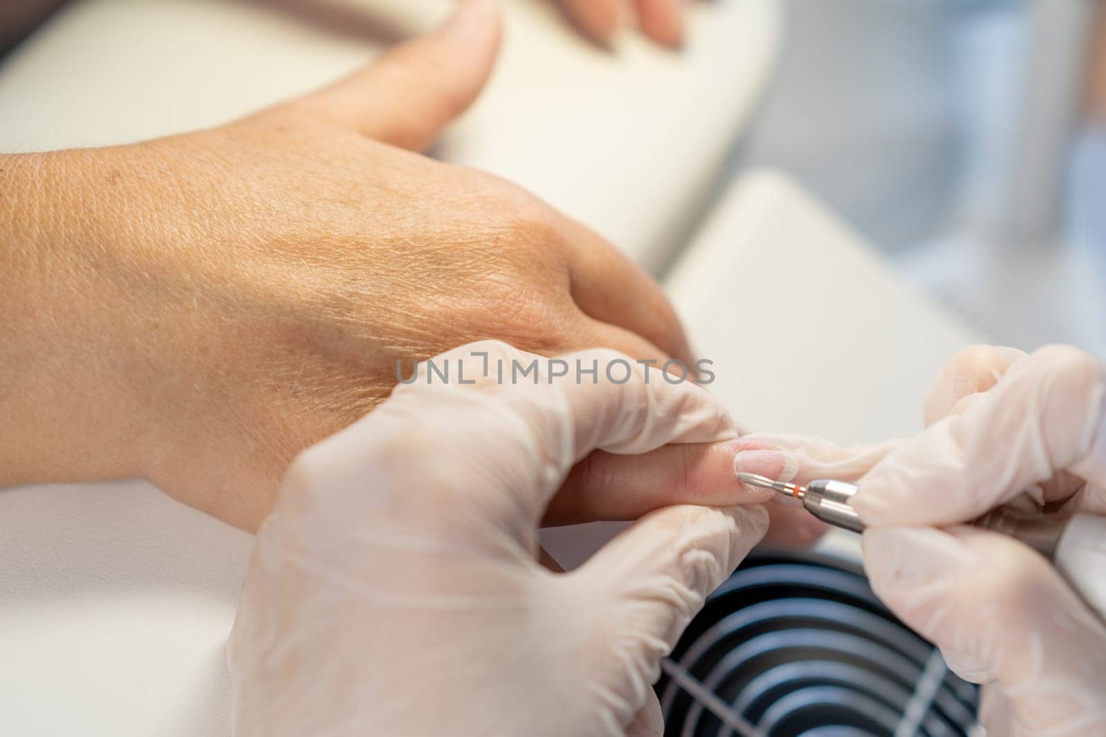 Nail care procedure in a beauty salon. Female hands and tools for manicure, process of performing manicure in beauty salon. Gloved hands of a skilled manicurist cutting cuticles. Concept spa body care
