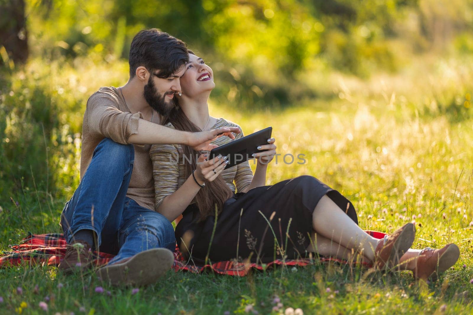 A young couple sits in nature and looks at something in a tablet