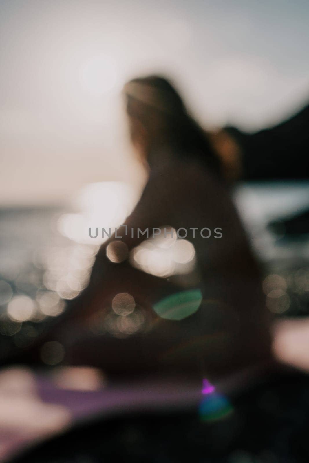 Abstract defocused silhoute of middle aged well looking woman with black hair doing Pilates with the ring on the yoga mat near the sea on the pebble beach. Female fitness yoga concept. by panophotograph