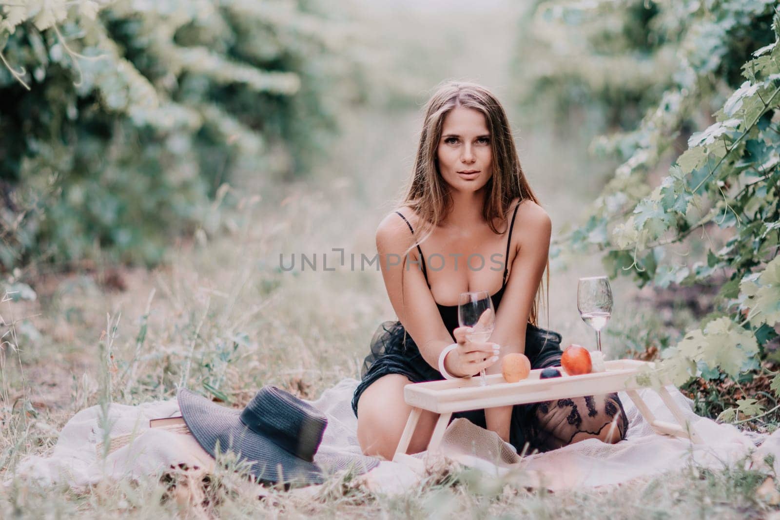 Woman picnic vineyard. Happy woman with a glass of wine at a picnic in the vineyard, wine tasting at sunset and open nature in the summer. Romantic dinner, fruit and wine. by panophotograph