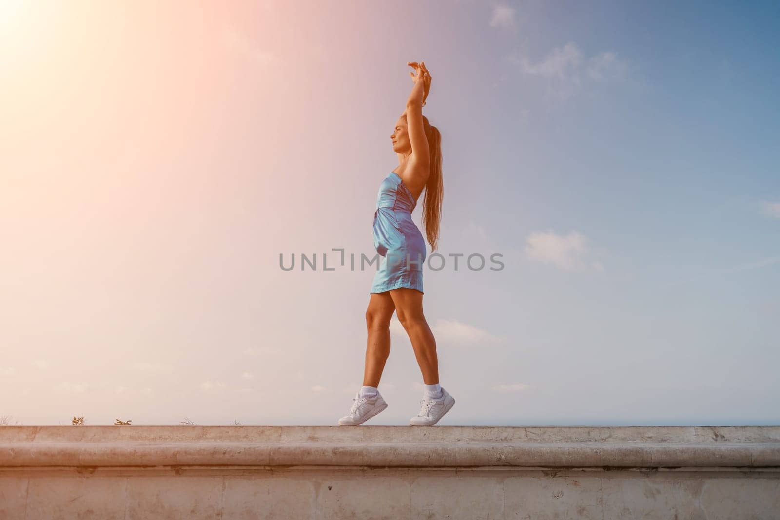 Woman travel sea. Happy tourist in blue dress takes a photo outdoors to capture memories. woman traveling and enjoying her surroundings on the beach, with volcanic mountains in the background. by panophotograph