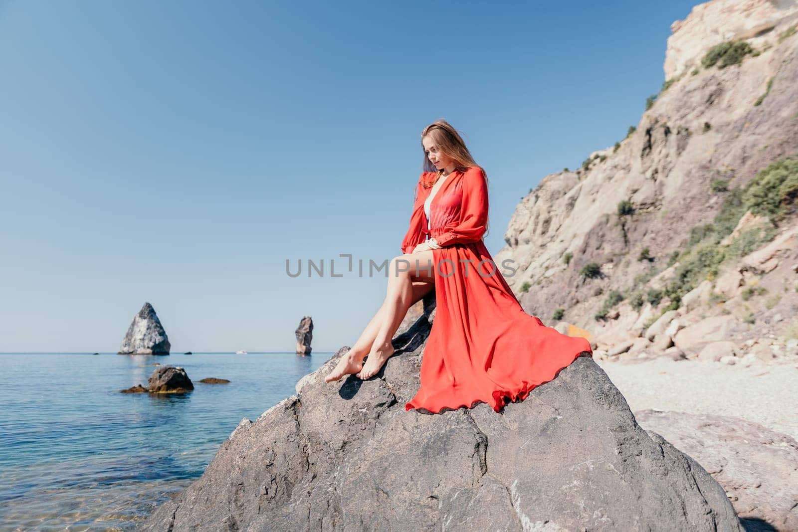 Woman travel sea. Young Happy woman in a long red dress posing on a beach near the sea on background of volcanic rocks, like in Iceland, sharing travel adventure journey by panophotograph