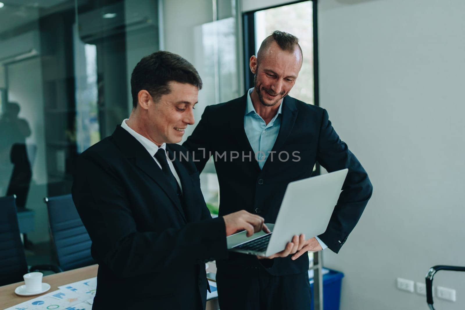 Two business men meeting to talking or discuss marketing work in workplace using paperwork, calculator, computer to work. by Manastrong