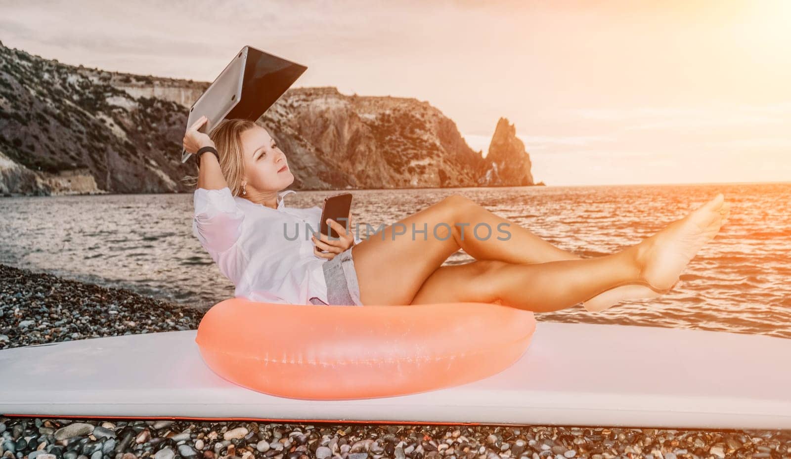 Successful business woman in yellow hat working on laptop by the sea. Pretty lady typing on computer at summer day outdoors. Freelance, travel and holidays concept.